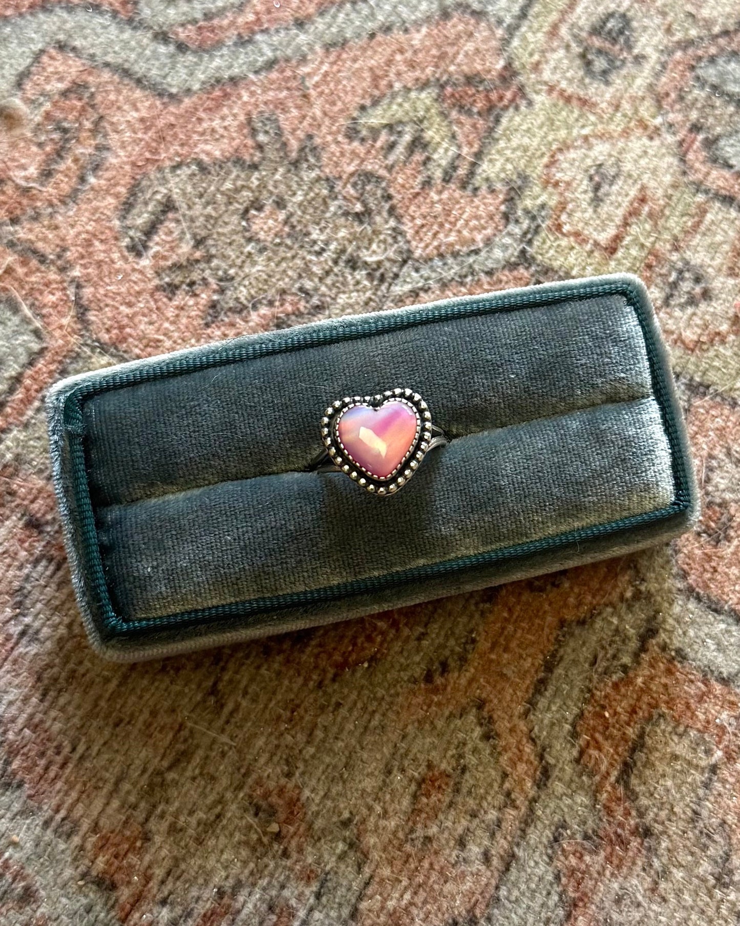 Black jewelry box with a pink heart on a patterned fabric background
