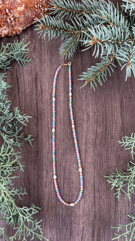 Multicolored beaded necklace on a wooden surface with greenery