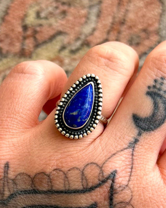 Hand wearing a ring with a blue stone on a tattooed arm