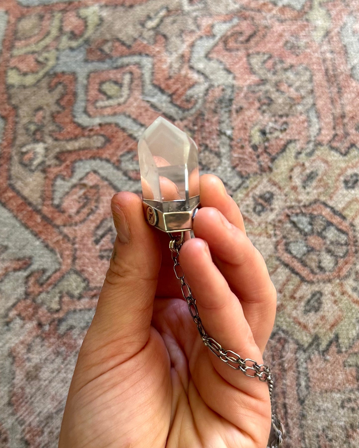 Hand holding a crystal pendant necklace against a patterned rug background