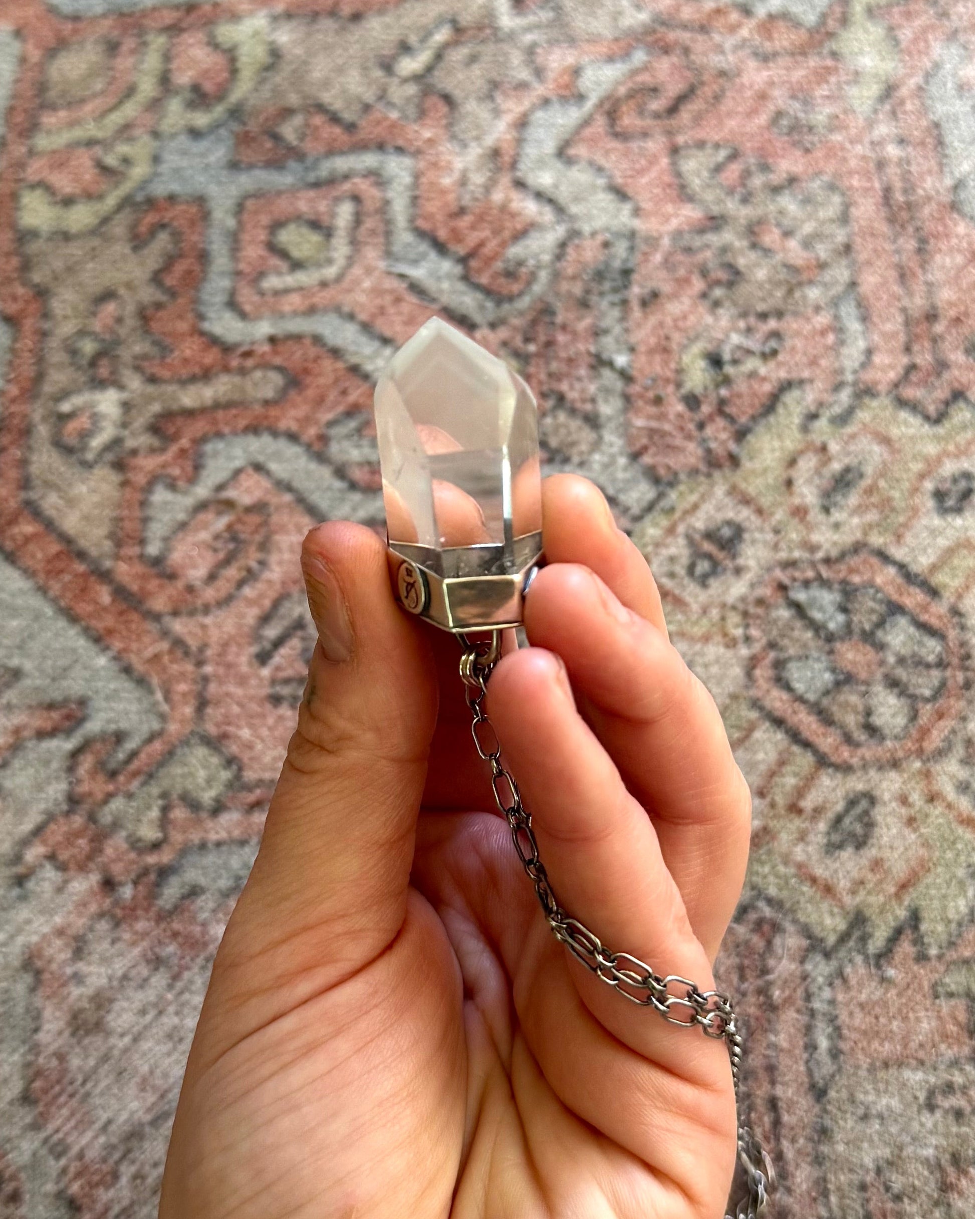 Hand holding a crystal pendant necklace against a patterned rug background