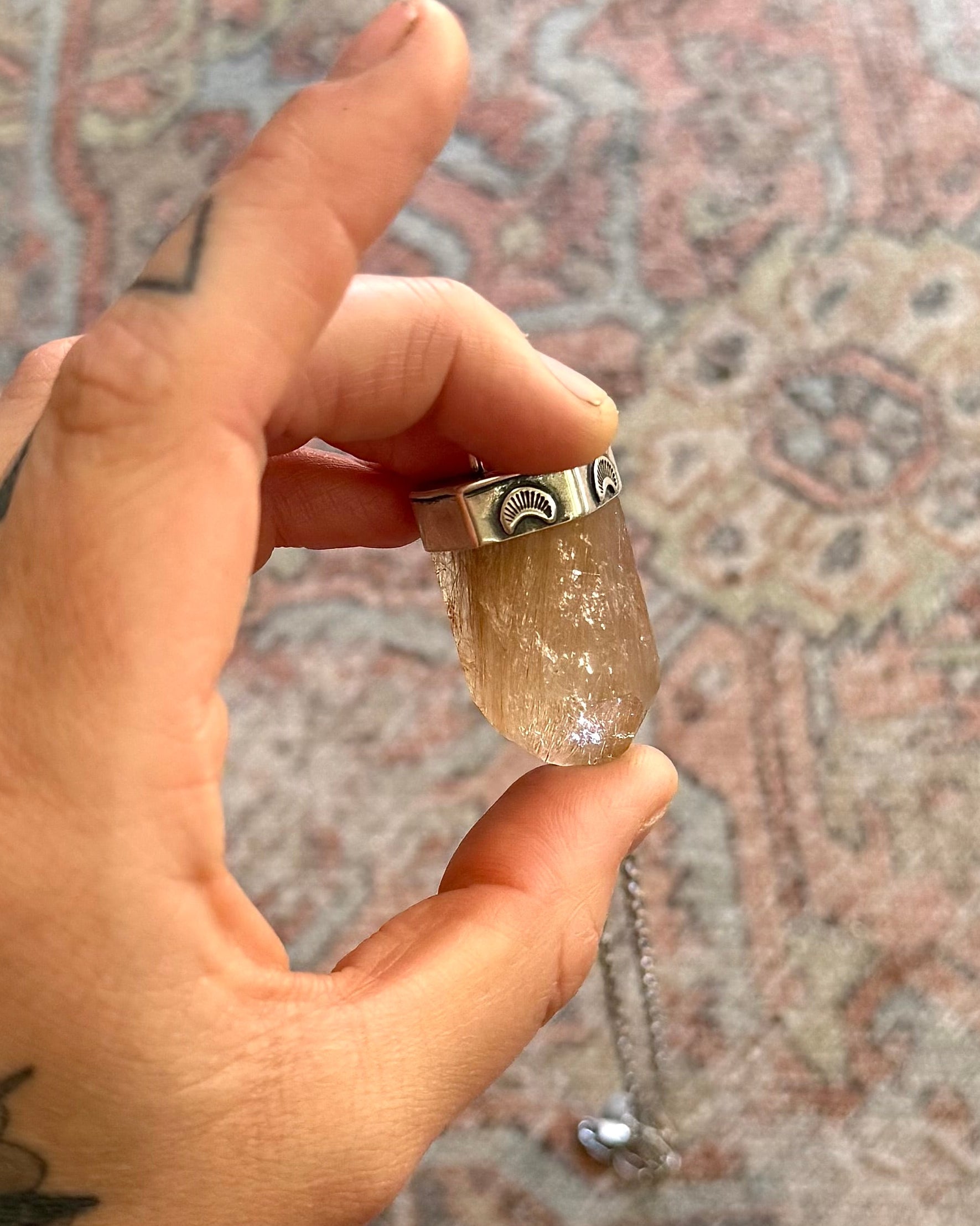 Hand holding a crystal pendant with a chain against a patterned rug background