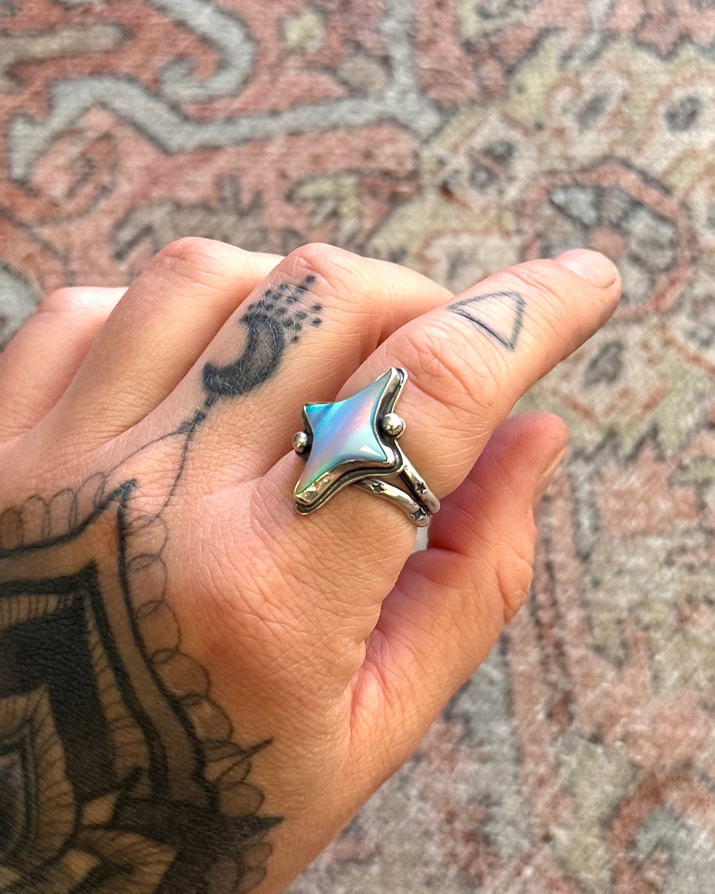Hand with a star-shaped ring on a patterned rug