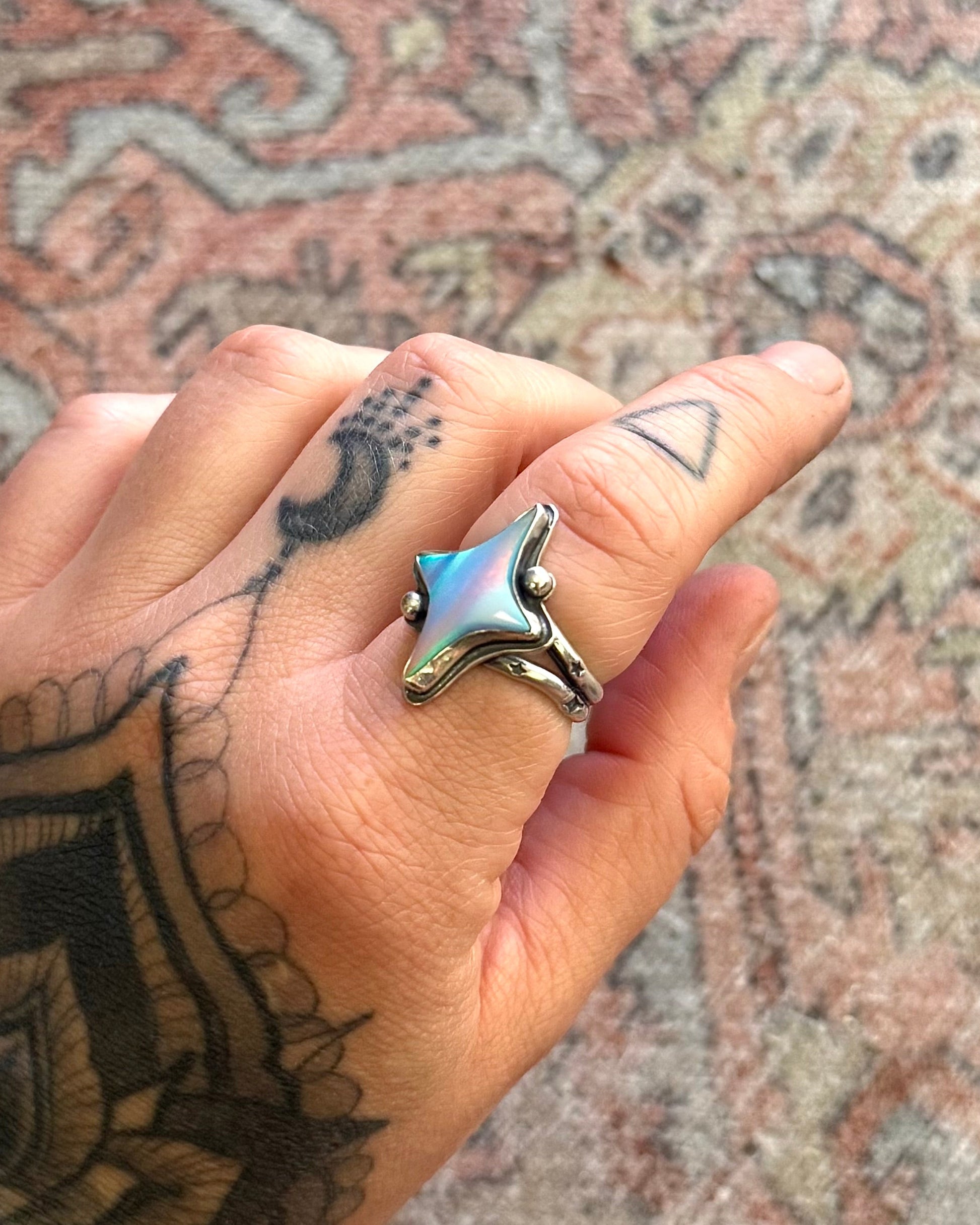 Hand with a star-shaped ring on a patterned rug