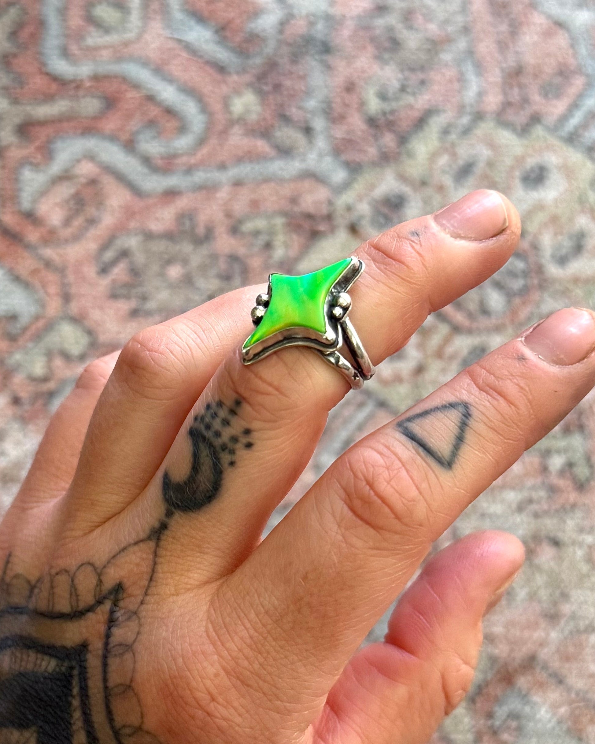 Hand with tattoos wearing a green and black ring on a patterned rug background