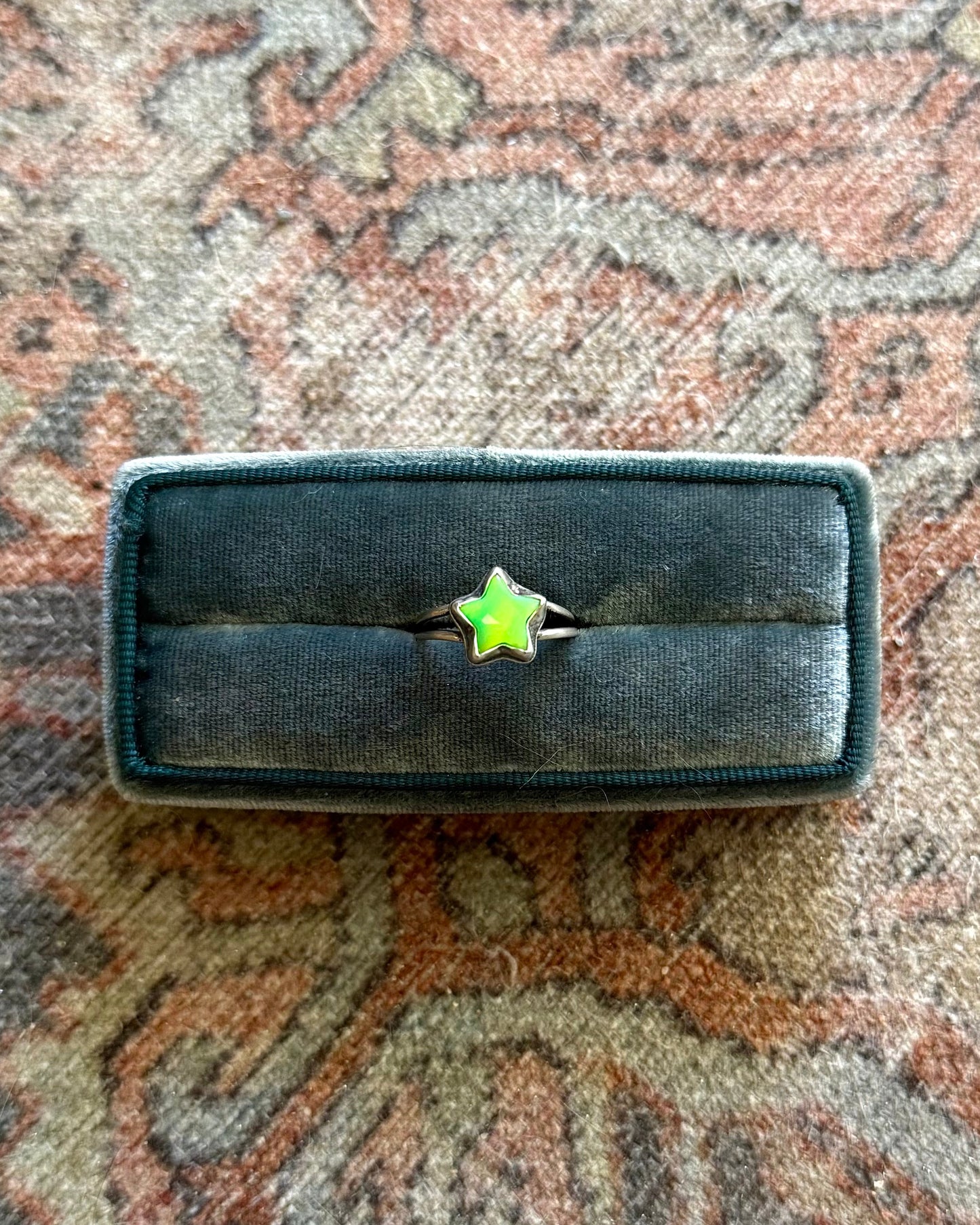 Ring with green gemstone in a box on a patterned rug