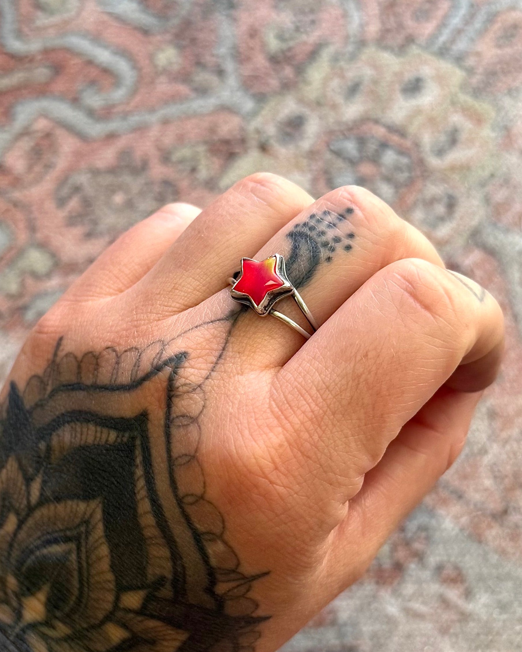 Hand with tattoos and a red ring on a patterned surface