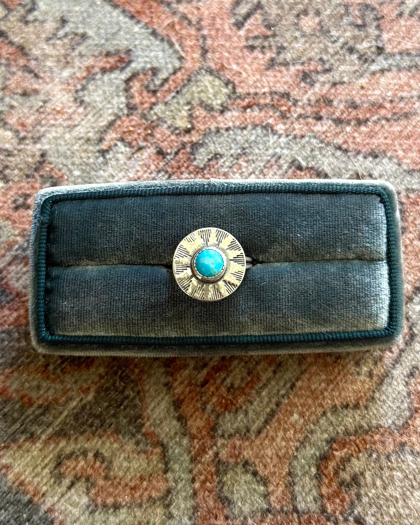 Black belt buckle with a turquoise stone on a patterned rug