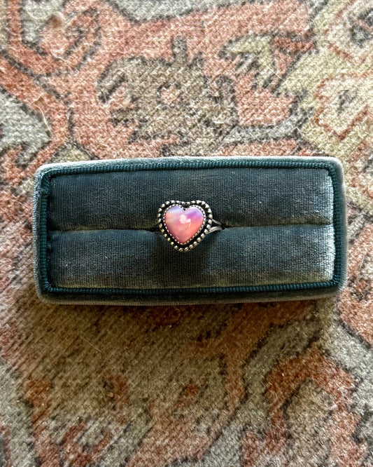 Black rectangular object with a pink heart on a patterned fabric background