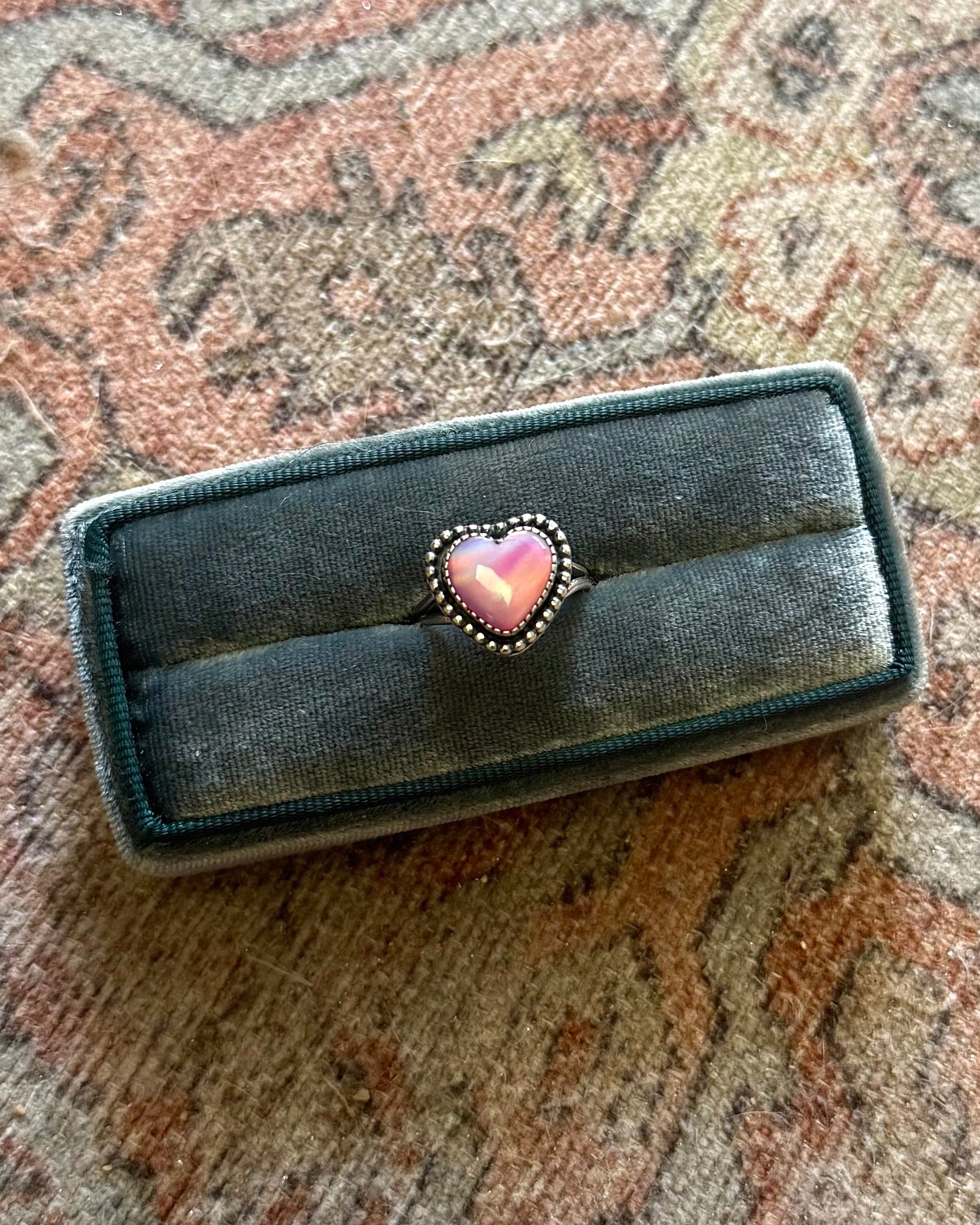 Black jewelry box with a pink heart on a patterned fabric background