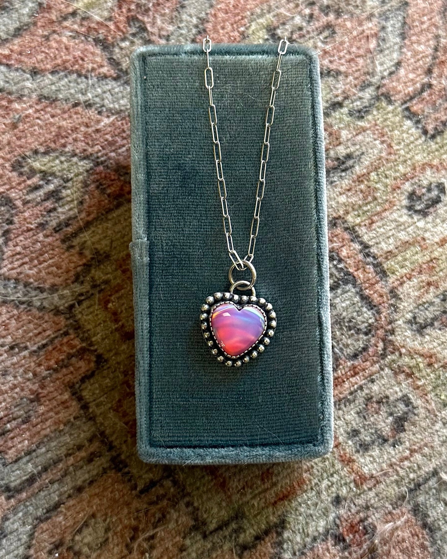 Necklace with a heart-shaped pendant in a box on a patterned fabric background