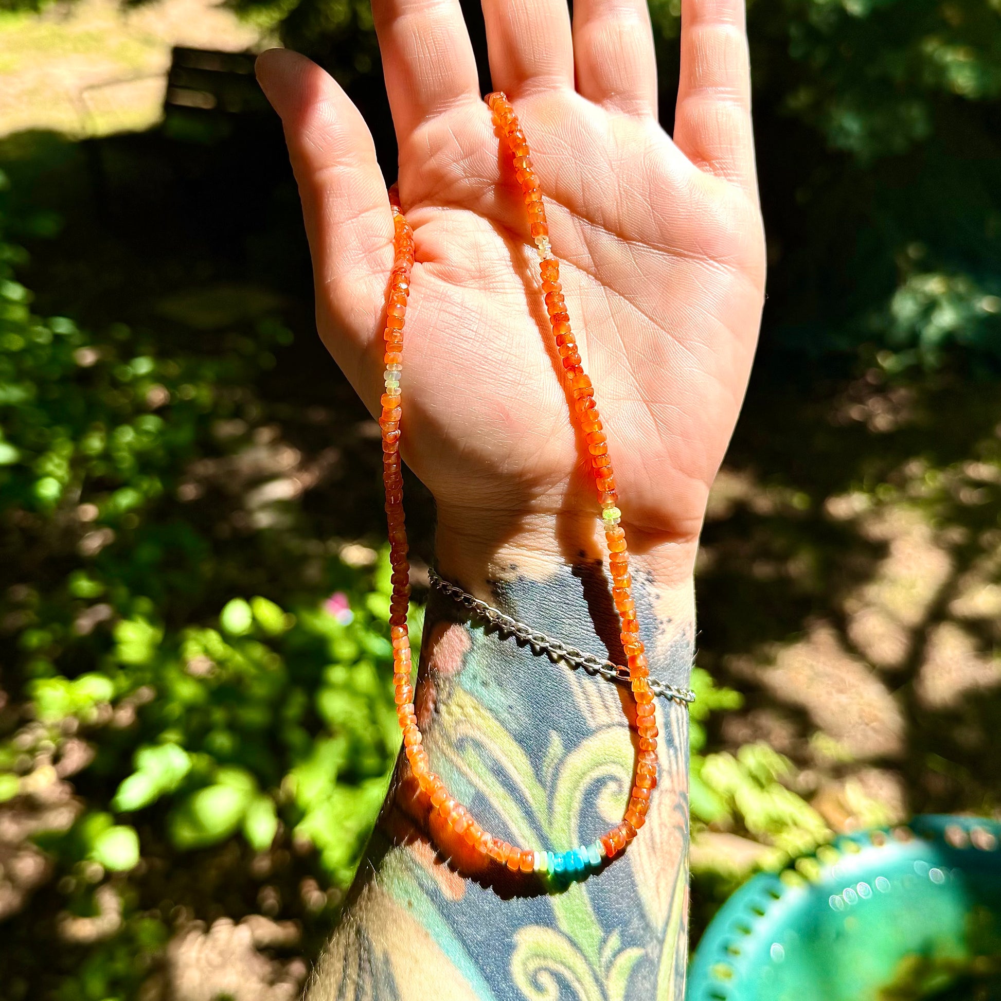 Hand holding a beaded necklace with a blurred natural background