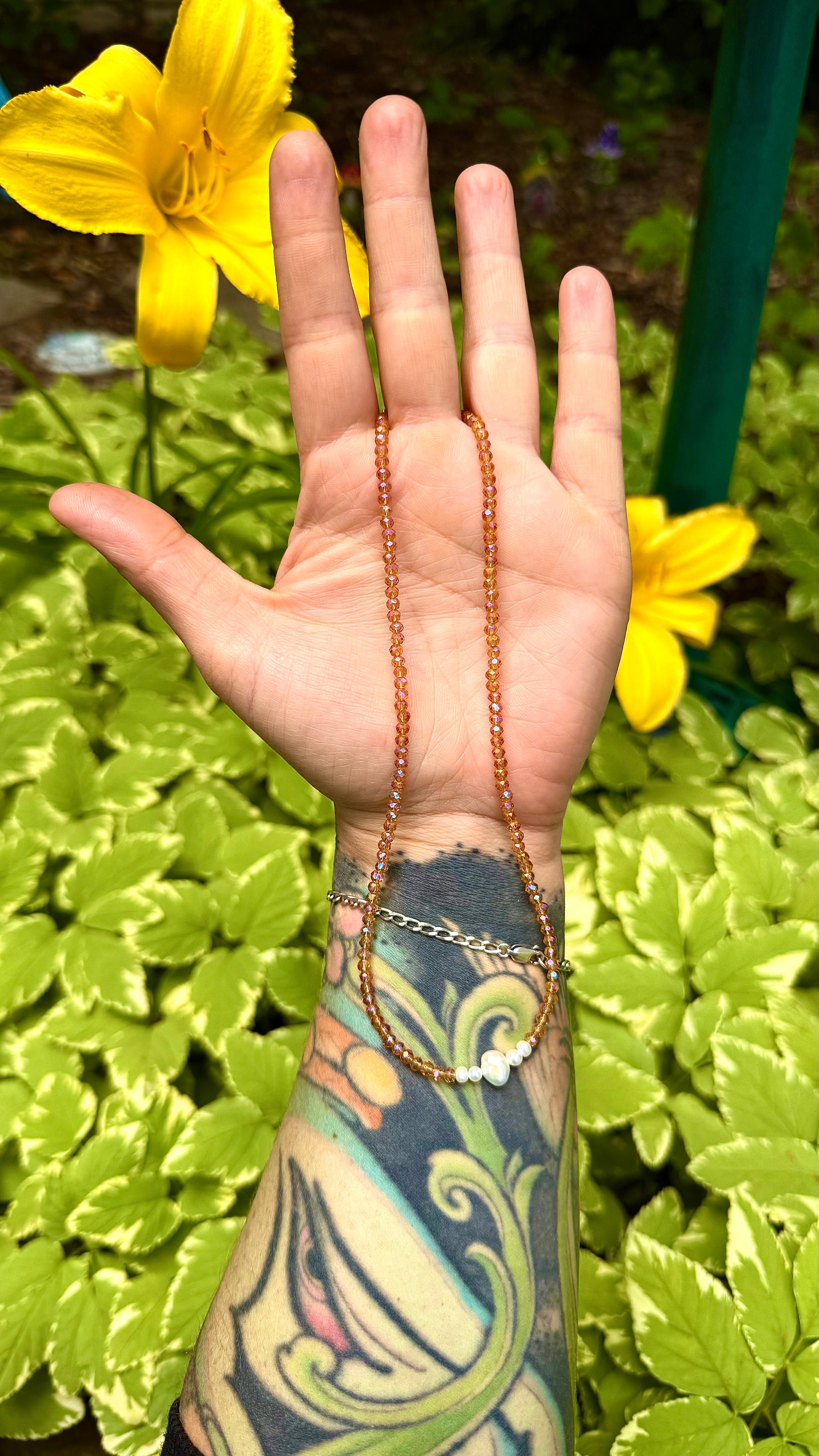Hand with a necklace against a green foliage background
