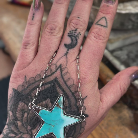 Kingman Turquoise Statement Necklace with a star-shaped turquoise pendant held in a tattooed hand, showcasing intricate chain details.