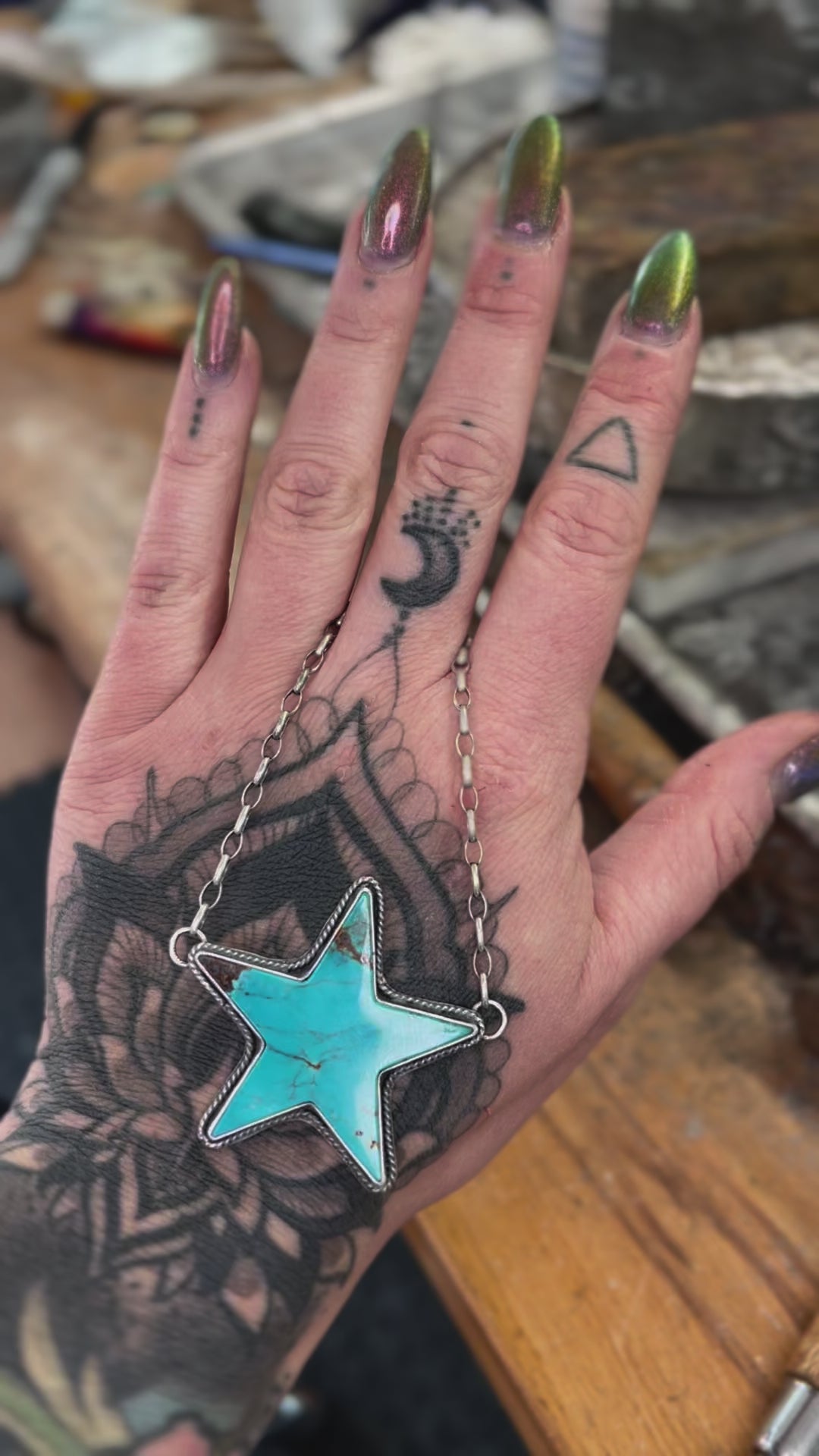 Kingman Turquoise Statement Necklace with a star-shaped turquoise pendant held in a tattooed hand, showcasing intricate chain details.